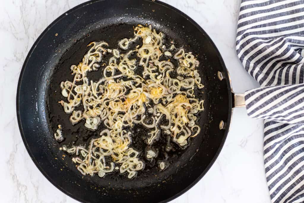 Thinly sliced shallots sautéing in a skillet with oil until golden.