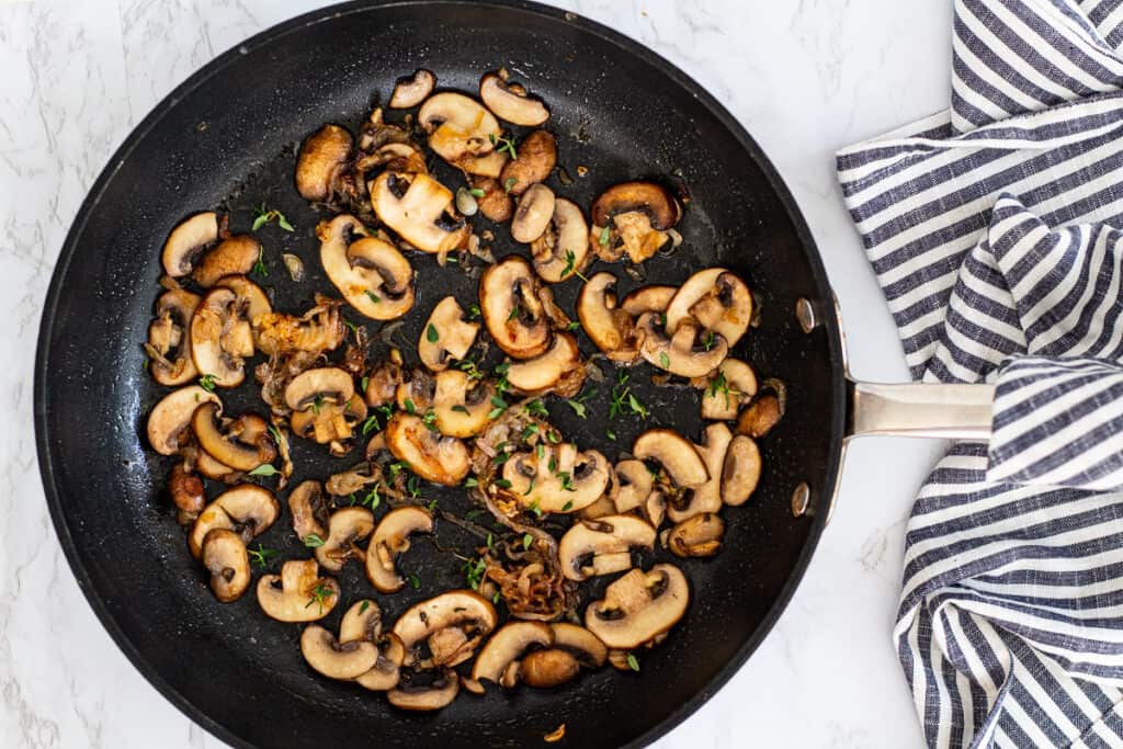 Mushrooms and shallots cooking together in a skillet with fresh thyme.