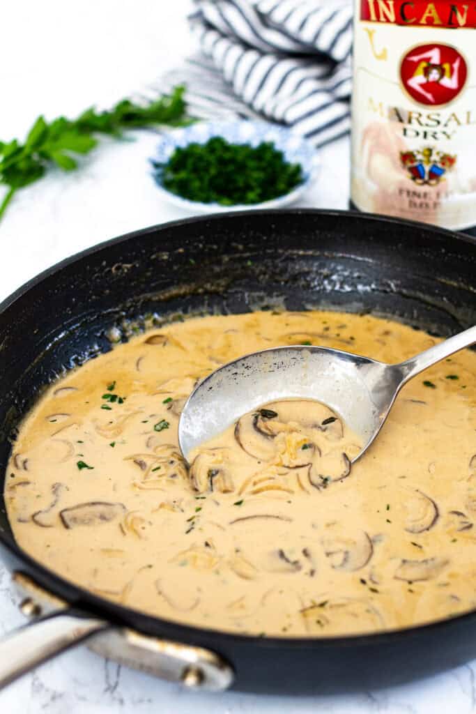 Finished marsala cream sauce in a black skillet with mushrooms and parsley.