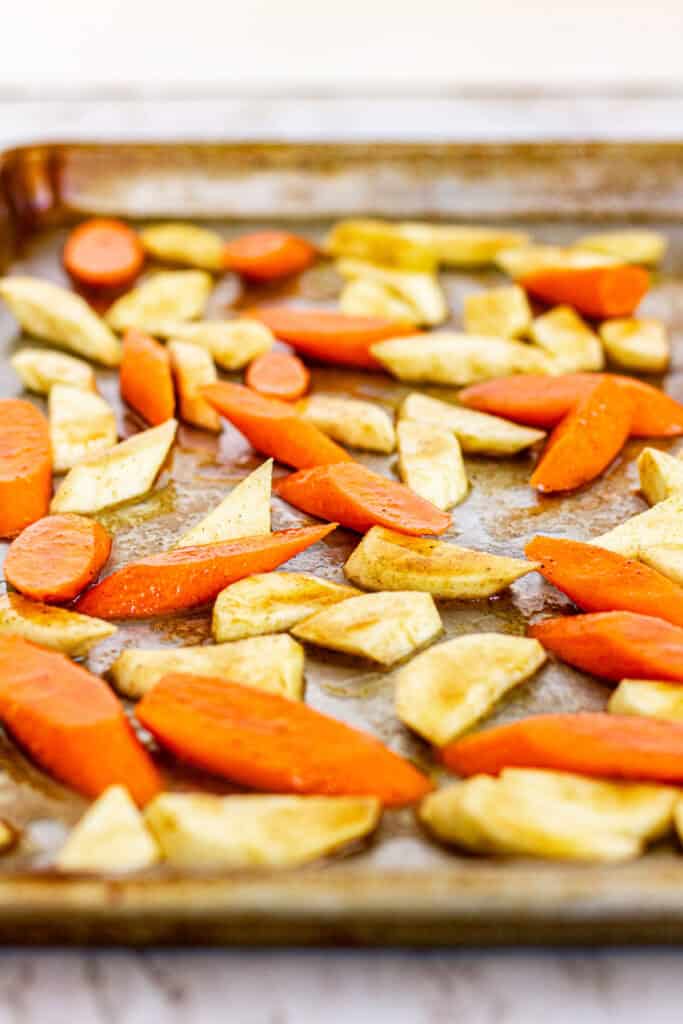Carrots and parsnips tossed with olive oil, butter, honey, and Moroccan spices on a baking sheet before roasting