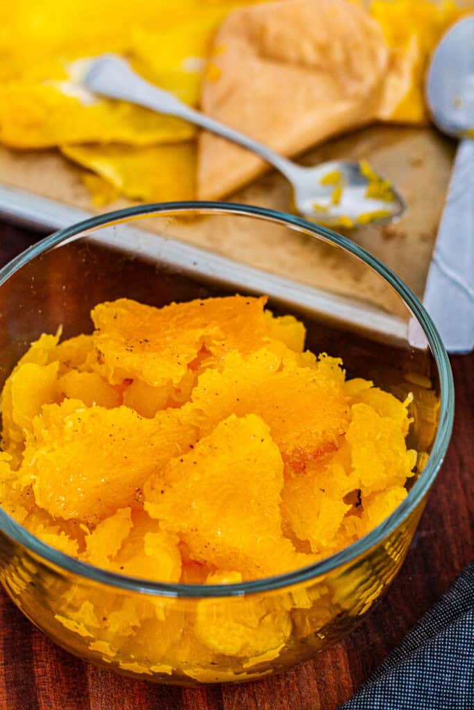 A glass bowl filled with scooped roasted butternut squash, ready to use in soups.