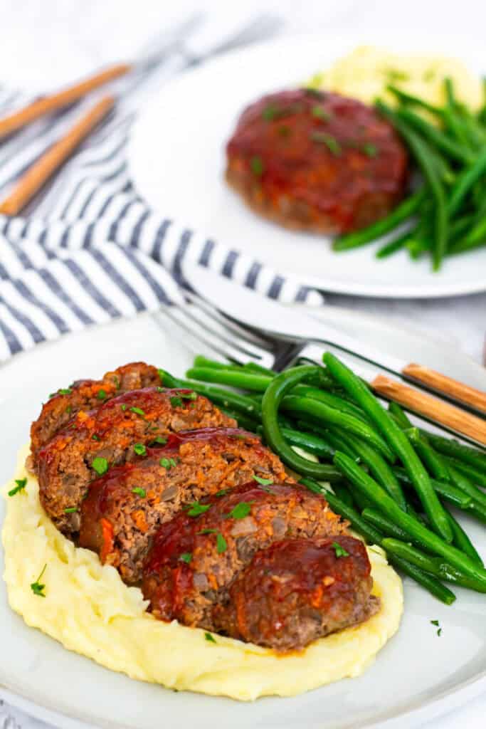 Sliced glazed mini meatloaf served with creamy mashed potatoes and sautéed green beans on a white plate