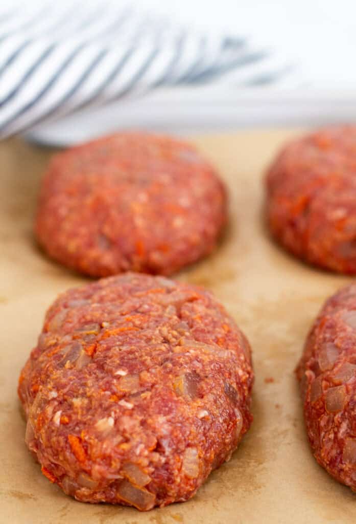 Uncooked mini meatloaf patties shaped by hand on a parchment-lined baking sheet