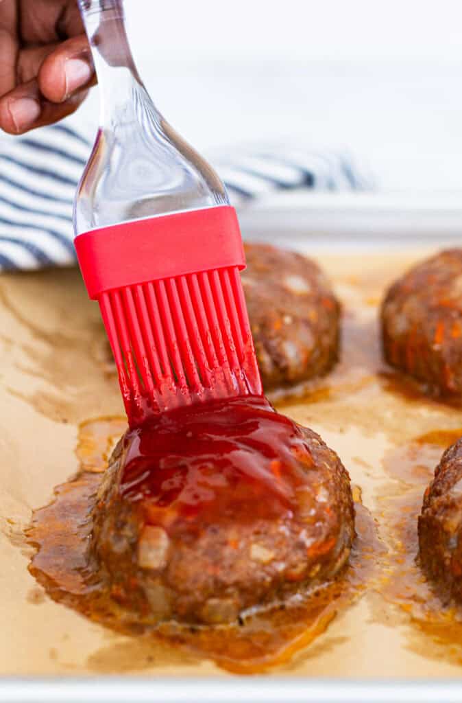 Hand brushing ketchup glaze over freshly baked mini meatloaf patties