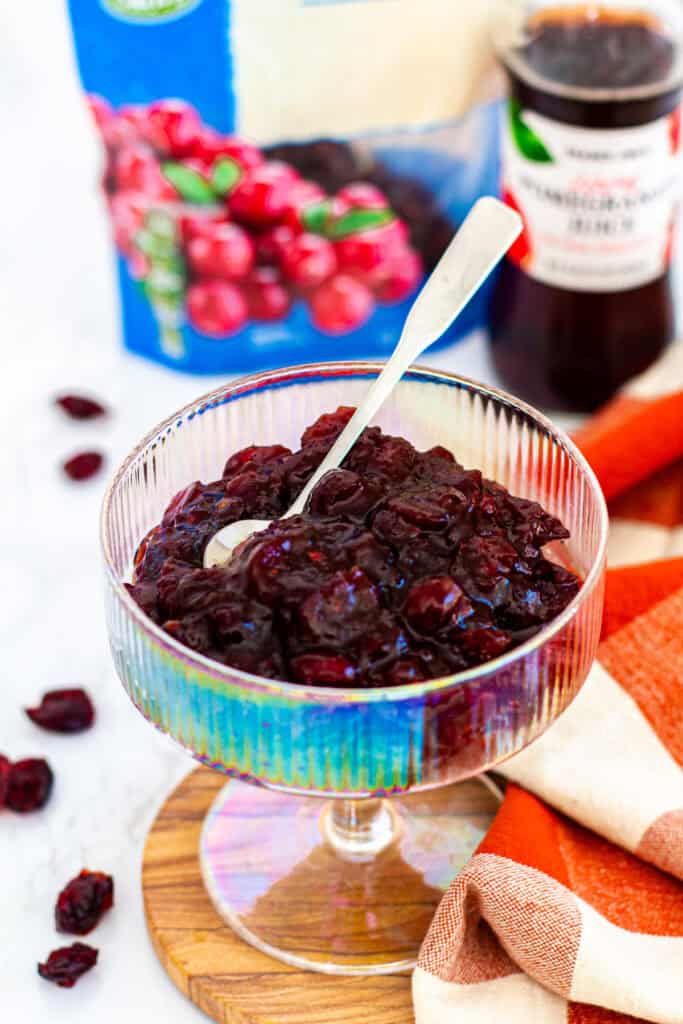 Cranberry sauce with dried cranberries in a clear glass dish, surrounded by juice and dried cranberry ingredients.