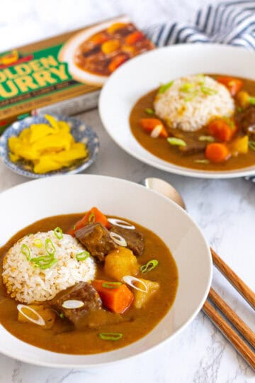 Two bowls of Japanese beef curry with rice and pickled yellow radish on the side.