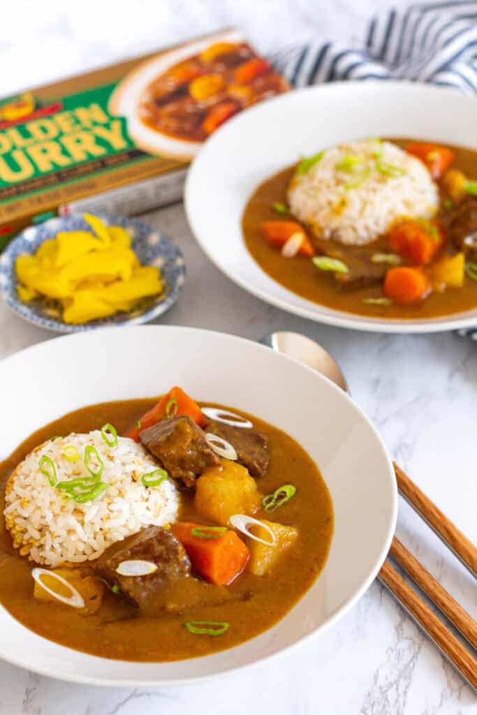 Two bowls of Japanese beef curry with rice and pickled yellow radish on the side.