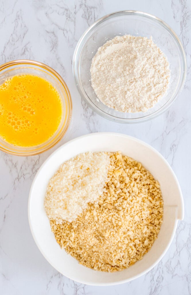 Overhead view of bowls with flour, beaten eggs, and parmesan panko mixture for coating mac and cheese bites.
