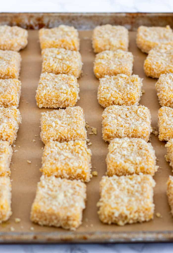 Panko and parmesan coated mac and cheese bite squares lined up on a parchment-lined tray.
