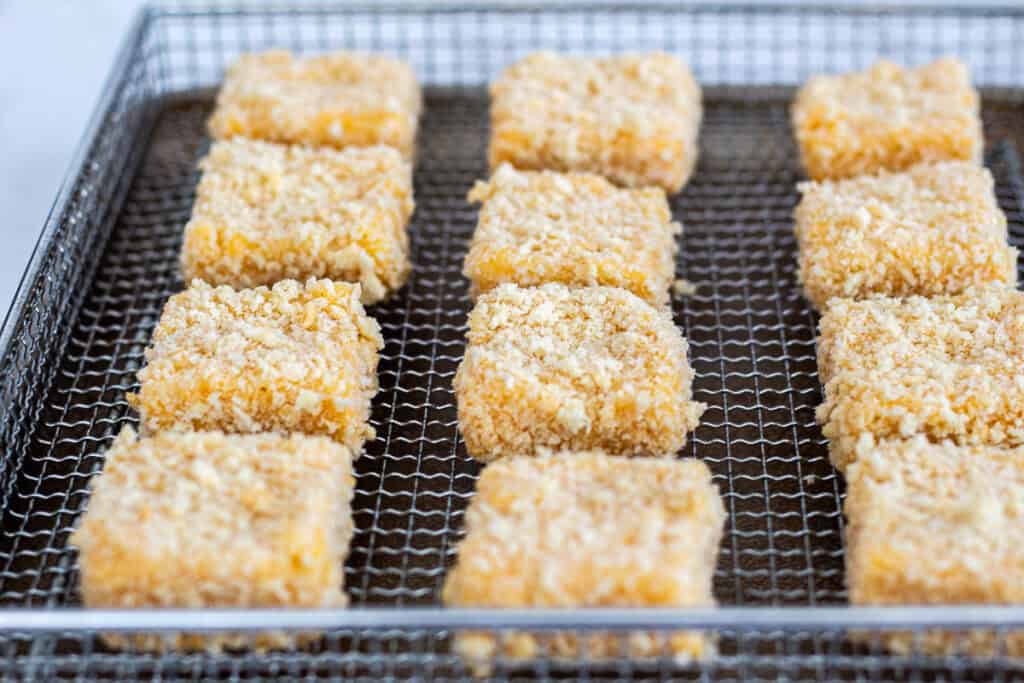 Breaded mac and cheese bites arranged in a single layer inside an air fryer basket.