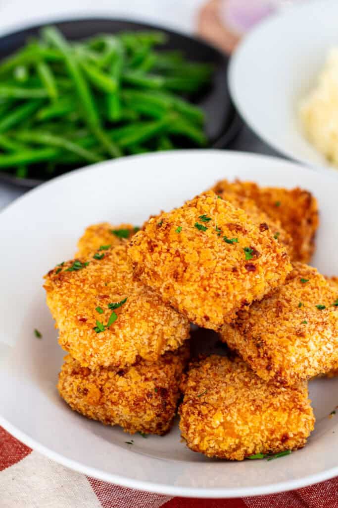 Plate of air fried mac and cheese bites garnished with parsley, served with green beans on the side.