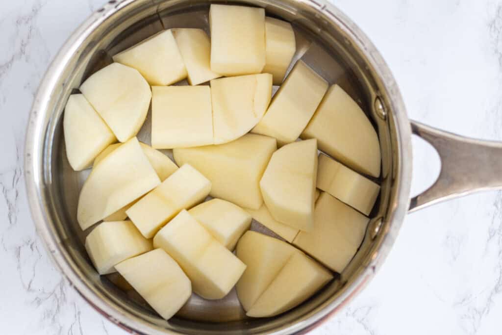 Raw russet potatoes cut into chunks in a stainless steel pot with water