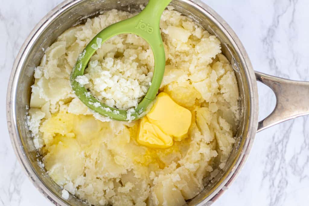 Pot of boiled potatoes with melted butter and a potato masher