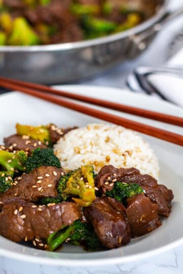 Close-up of glossy beef and broccoli in sauce with rice and sesame seeds, showing tender texture.