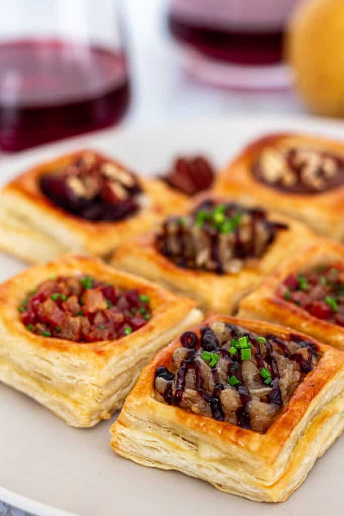 Flaky puff pastry squares filled with brie and toppings like caramelized onions, nuts, and jam, perfect for a small Thanksgiving appetizer spread.
