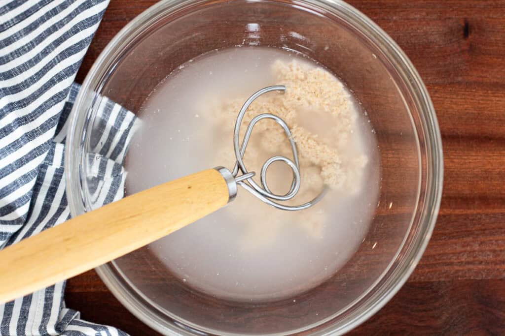 Sourdough discard being whisked into water to start cranberry walnut bread dough.