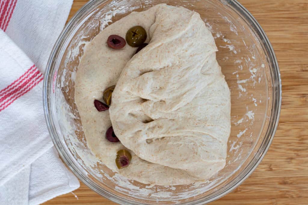 Chopped olives being folded into the dough during the bowl fold stage