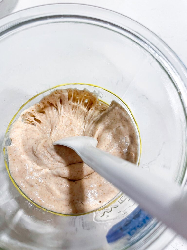 Close-up of a spoon stretching and mixing a young sourdough starter, showing texture and fermentation activity helpful for sourdough beginners.