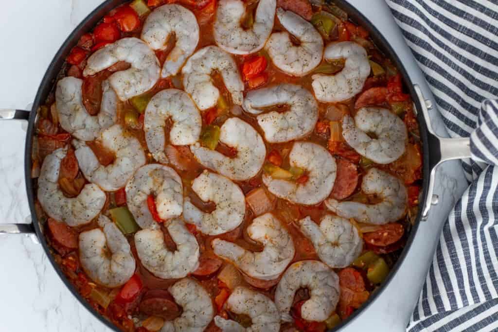 Raw shrimp arranged over simmering Cajun sausage stew before cooking.