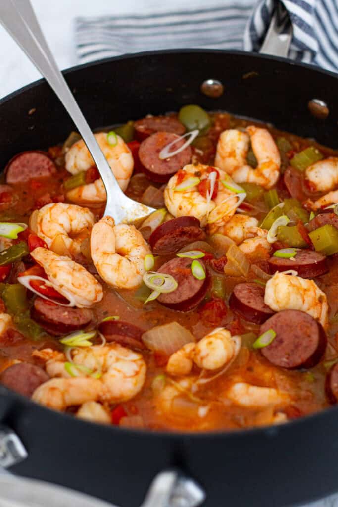 Cajun sausage and shrimp stew simmering in a skillet with tomatoes, peppers, and celery.