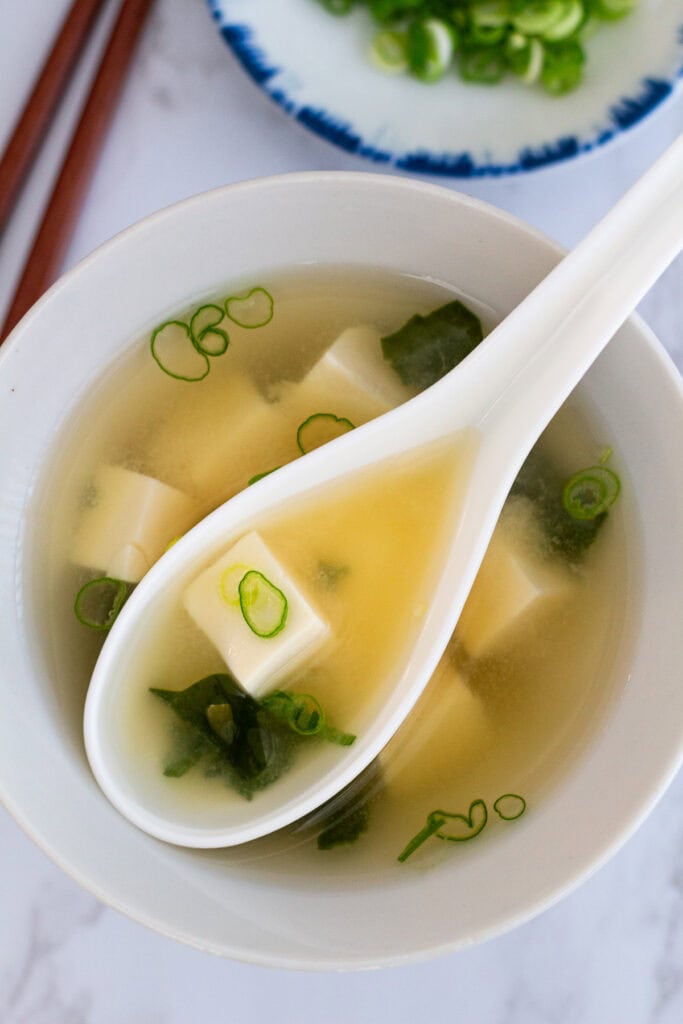 Close-up of miso soup with dashi showing silken tofu, wakame seaweed, and scallions in clear broth
