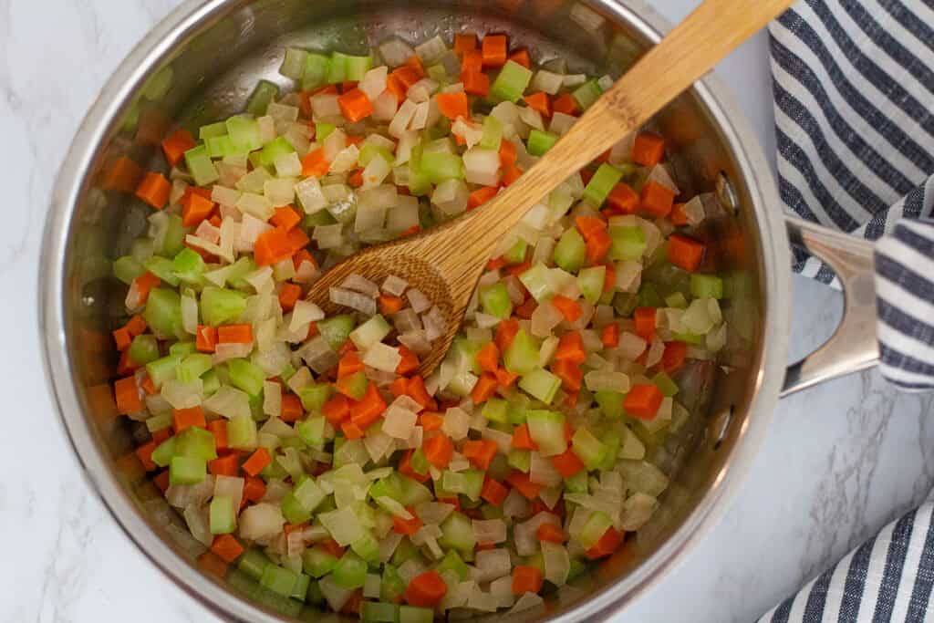 Diced onion, carrot, and celery softened in a pot with a wooden spoon.