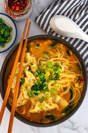 Overhead view of spicy miso dumpling noodle soup served with noodles, dumplings, and green onions.