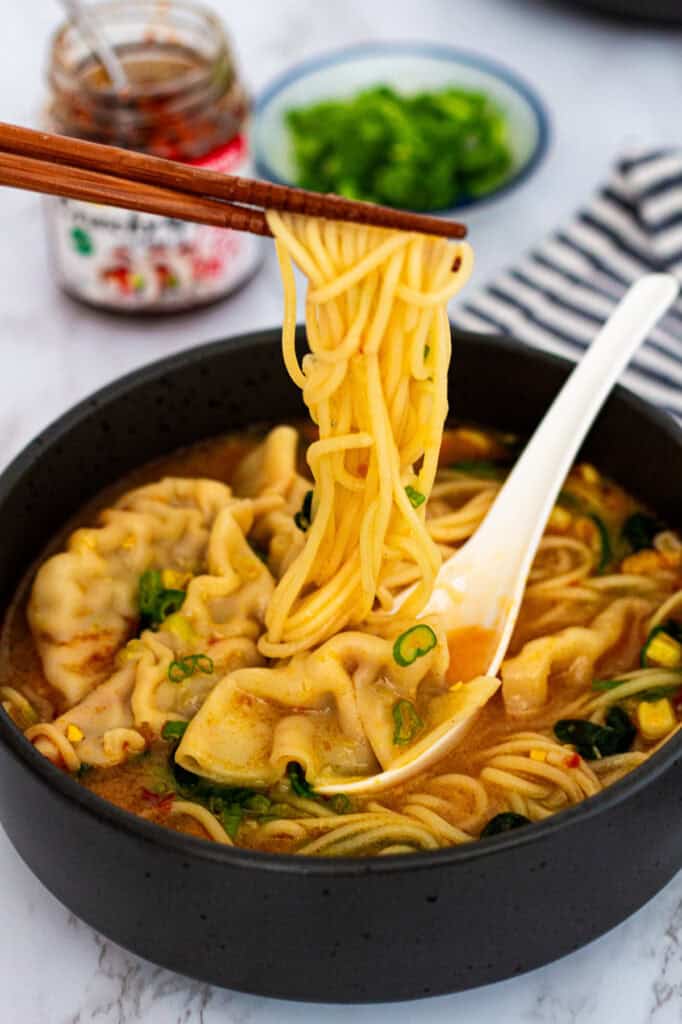 Chopsticks lifting noodles from a bowl of dumpling noodle soup with dumplings in spicy miso broth.