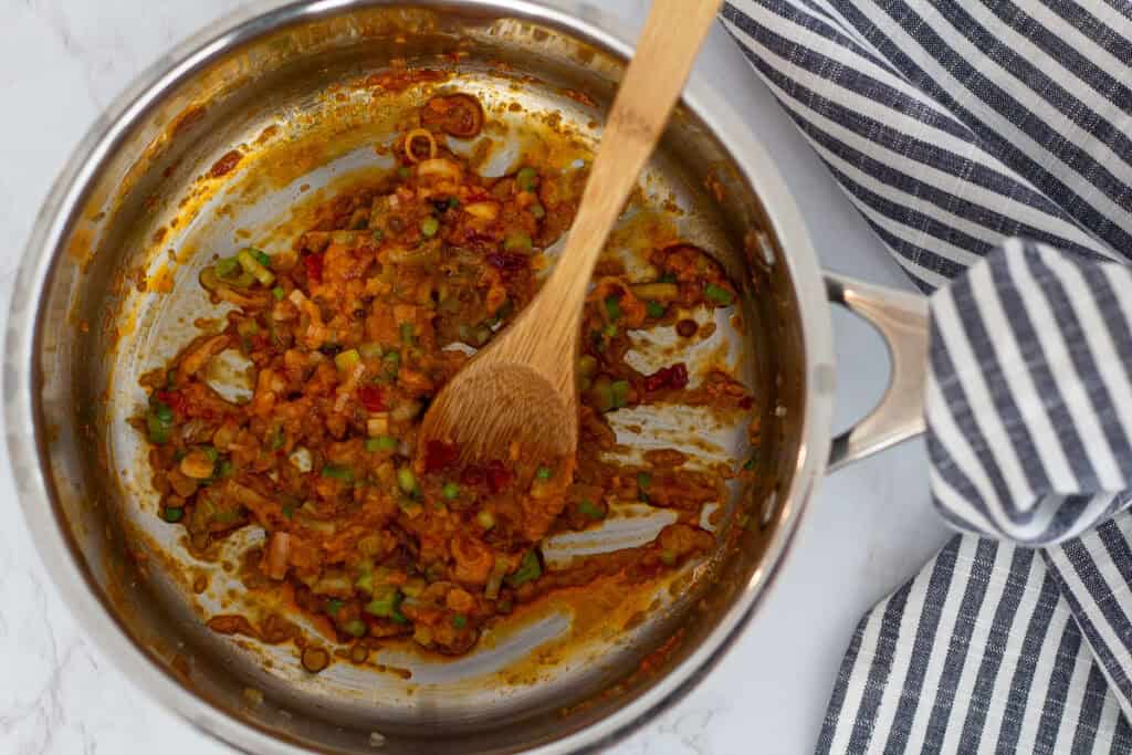 Miso paste and doubanjiang blooming with aromatics in a pot for a flavorful soup broth.