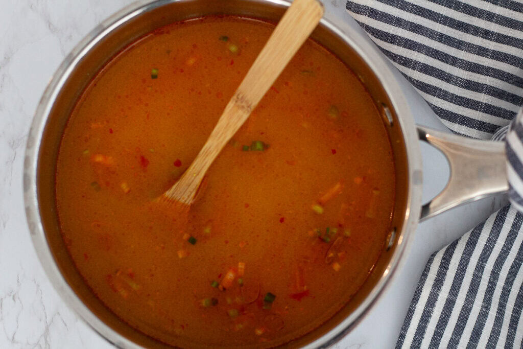 Spicy miso broth simmering in a pot for dumpling noodle soup.