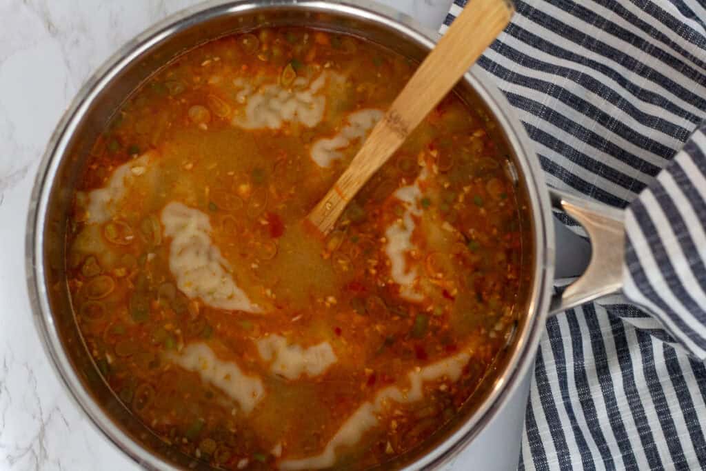Frozen dumplings cooking in a pot of spicy miso broth for dumpling noodle soup.