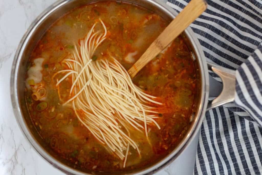 Fresh noodles added directly to the pot while cooking dumpling noodle soup.