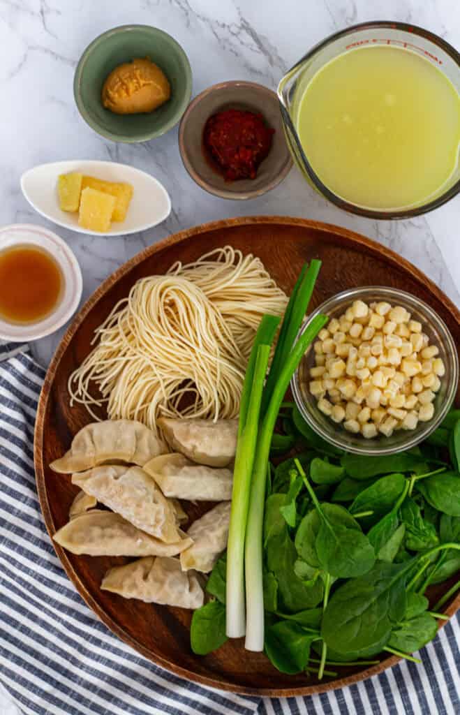 Ingredients for dumpling noodle soup including dumplings, fresh noodles, spinach, corn, miso, and broth.