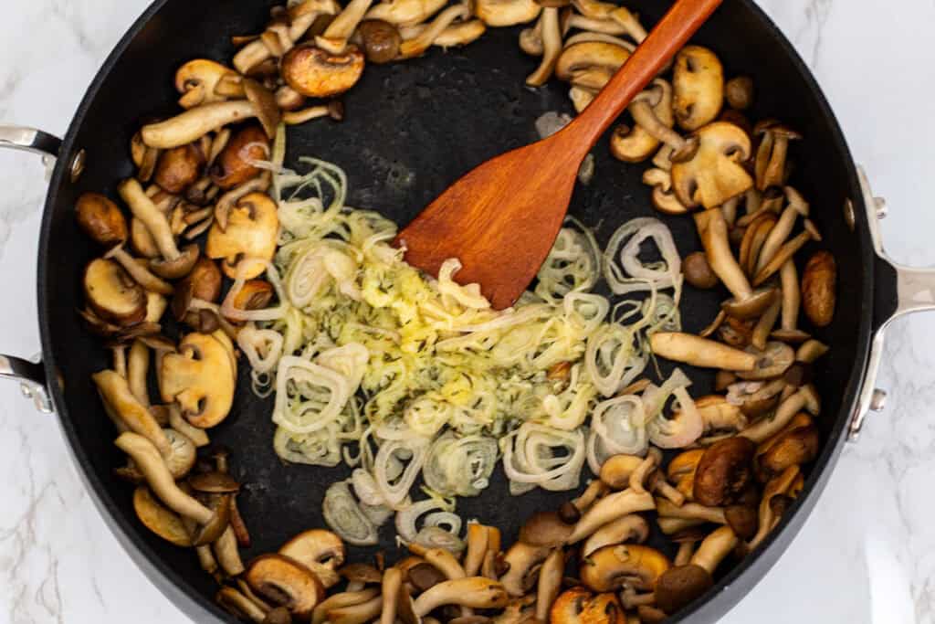 Shallots, garlic, and dried thyme cooking in the center of the pan with browned mushrooms pushed to the sides