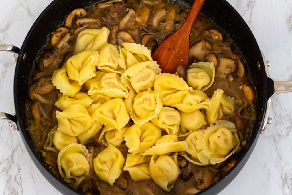 Cooked cheese tortellini added to the mushroom sauce to finish cooking in the pan
