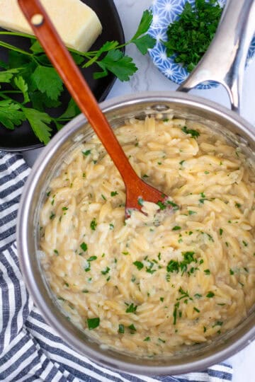 Creamy parmesan orzo in a saucepan, stirred with a wooden spoon while still glossy and smooth