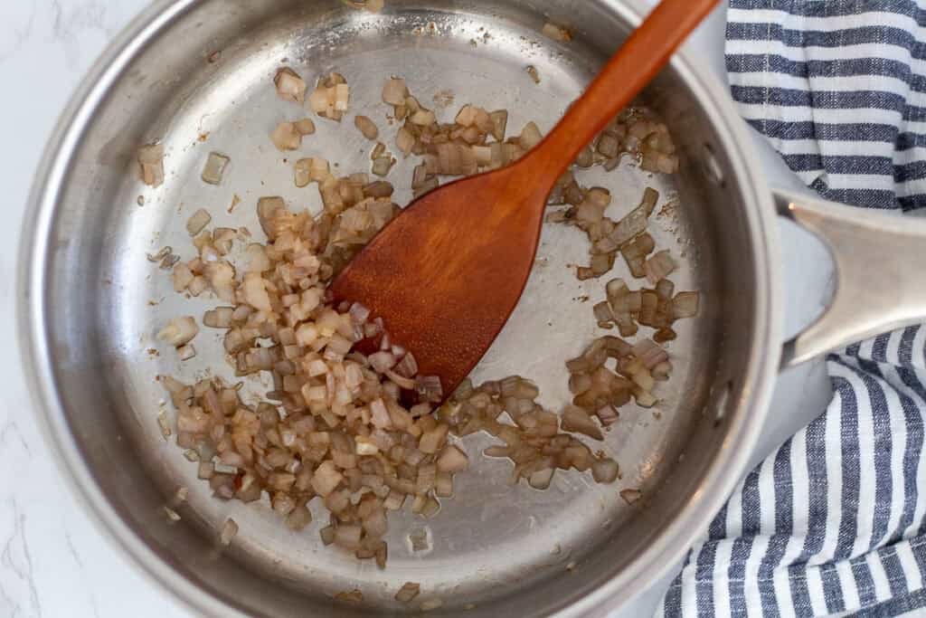 Finely chopped shallots sautéing in butter in a stainless steel pan for parmesan orzo