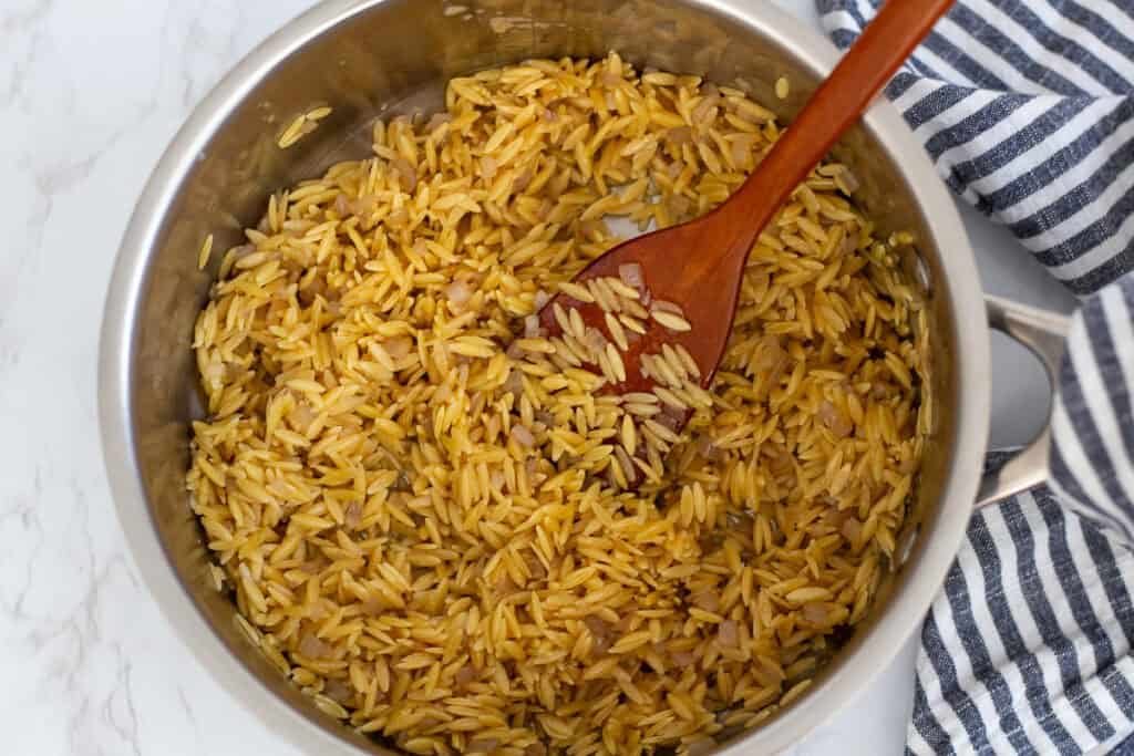 Orzo pasta being toasted in butter with shallots in a saucepan before adding liquid
