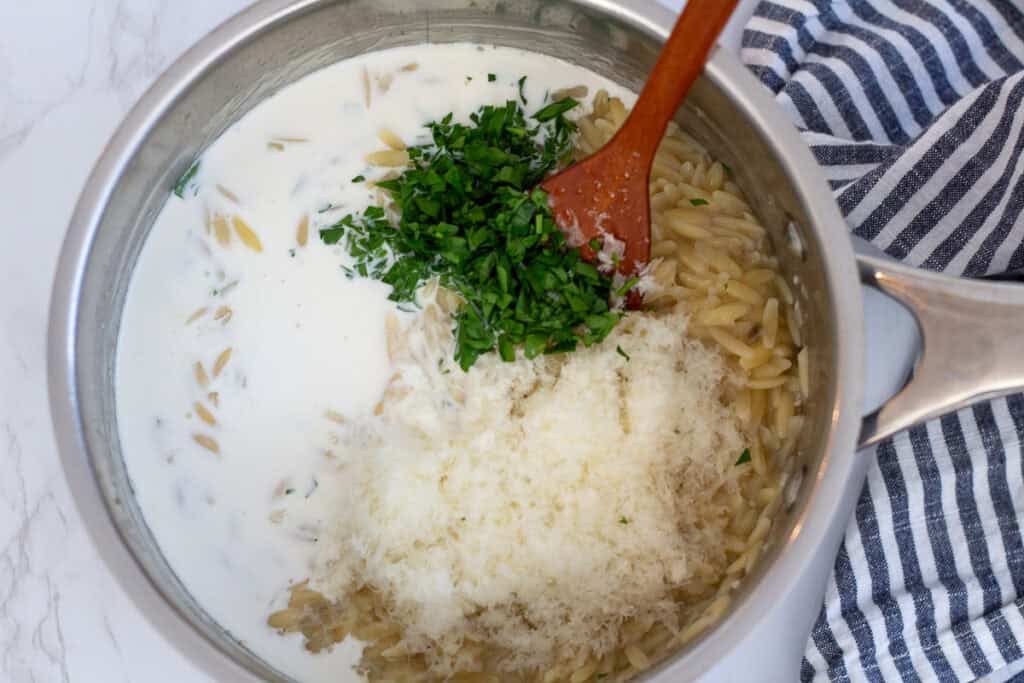 Heavy cream, freshly grated parmesan, and parsley added to cooked orzo in a saucepan