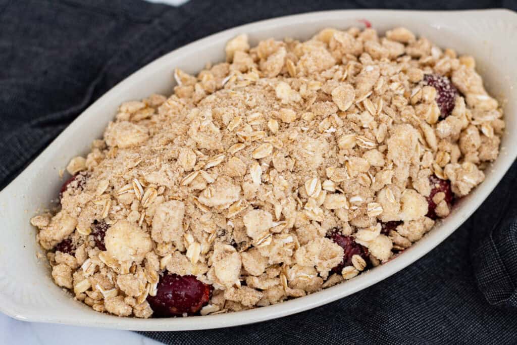 Unbaked cherry crisp topped with oat crumble in a small oval baking dish