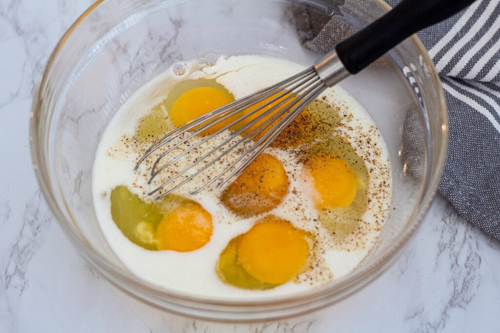 Eggs, milk, salt, and pepper in a bowl before whisking for leek frittata.