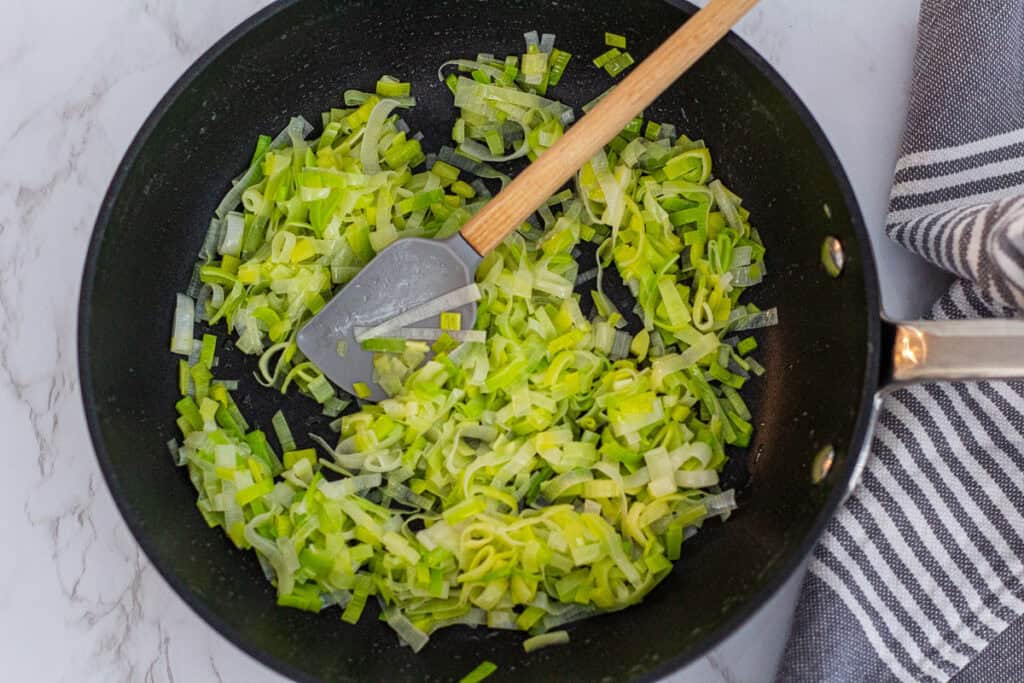 Thinly sliced leeks cooking in a skillet until soft for leek frittata.