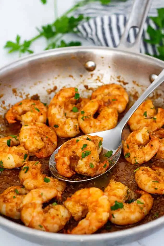 Spicy garlic butter shrimp garnished with chopped parsley in a skillet.