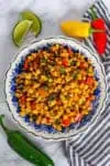 Simple skillet sautéed corn with bell peppers served on a plate with lime wedges and peppers
