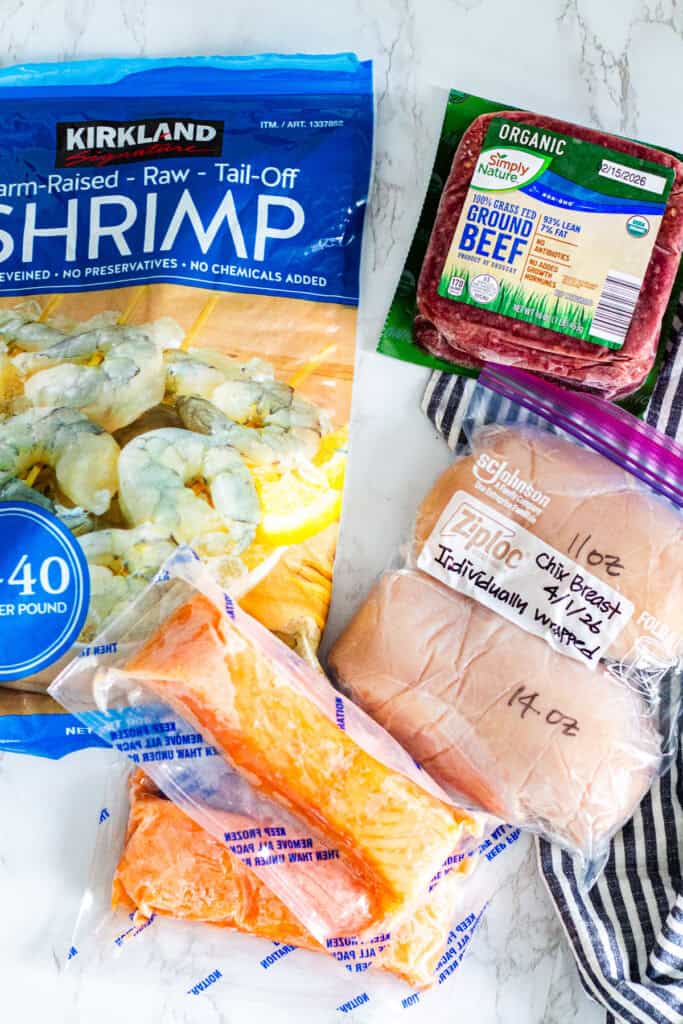 Different proteins including shrimp, ground beef, chicken breast, and salmon portioned and stored for a meal planning system for two