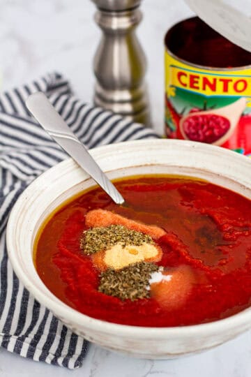 Crushed tomatoes with olive oil and dried spices in a bowl before mixing into no cook pizza sauce
