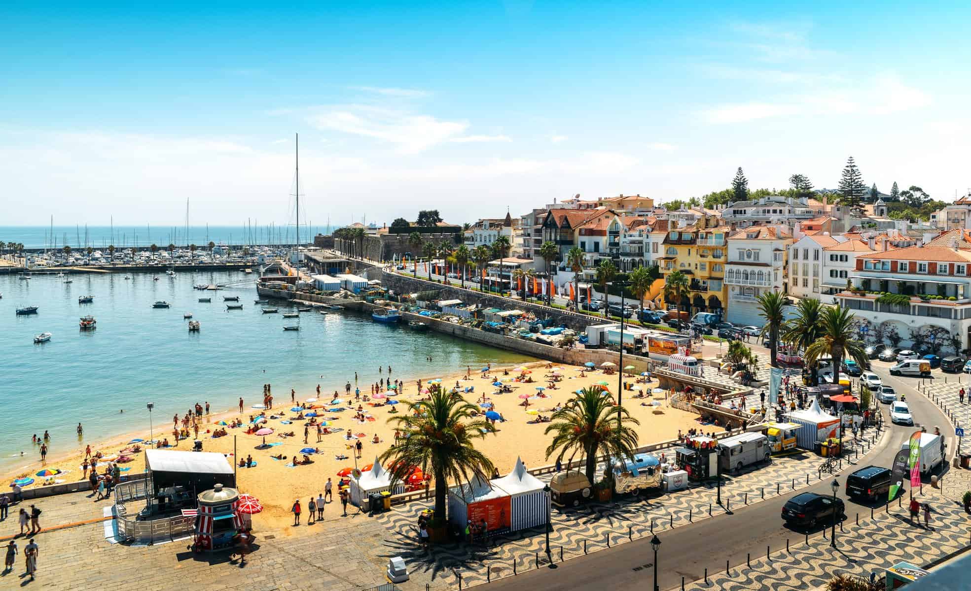 Cascais, Portugal - August 24, 2018: High vantage point of crowded sandy Praia do Ribeiro and boats on bay a a sunny summer day. Cascais is a small quaint village 30km west of Lisbon