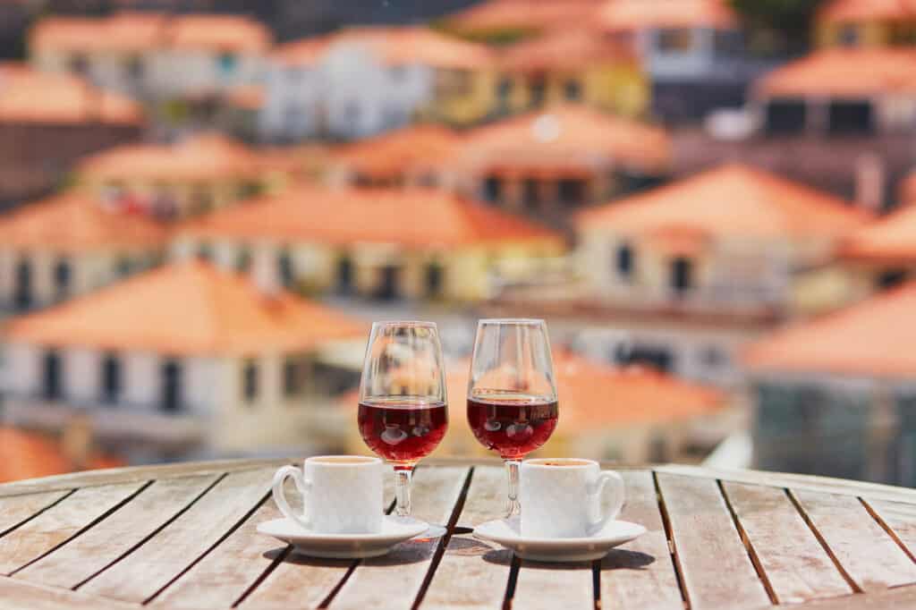 Two glasses of Madeira wine and two cups of fresh espresso coffee in street cafe with view to Funchal town, Madeira, Portugal