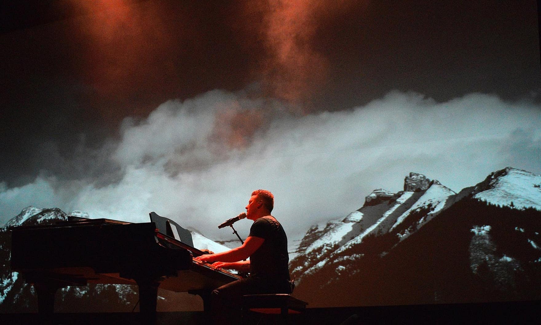 Musician playing piano on stage with mountain backdrop at NLW International event.
