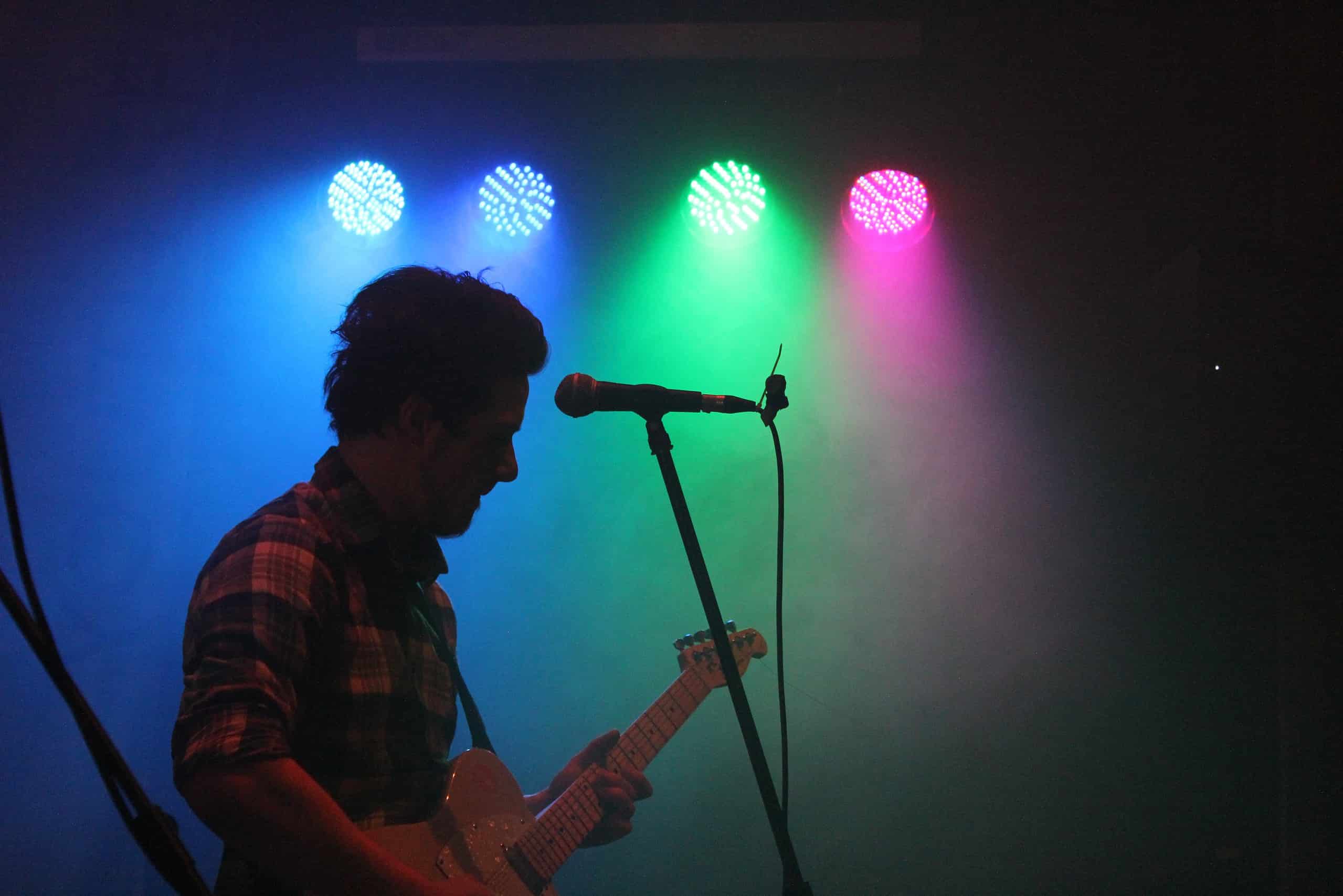 Worship musician playing guitar on stage with colorful lights at NLW International event.